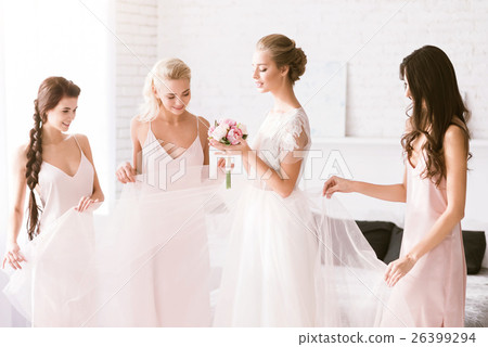 Amused bridesmaids touching the dress of the bride 26399294