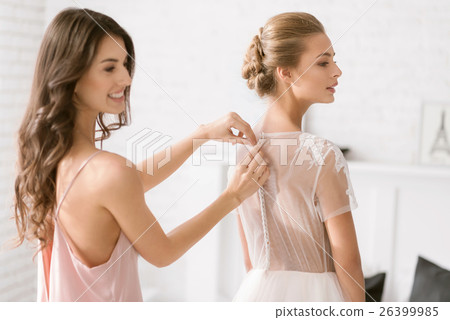Cheerful bridesmaid helping the bride with her 26399985