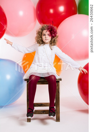 Girl sitting on a chair on a background of big colorful balloons Girl sitting on a chair on a background of big colorful balloons 26430662