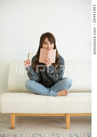 A young lady who reads while drinking champagne on the sofa in the living room 26441981