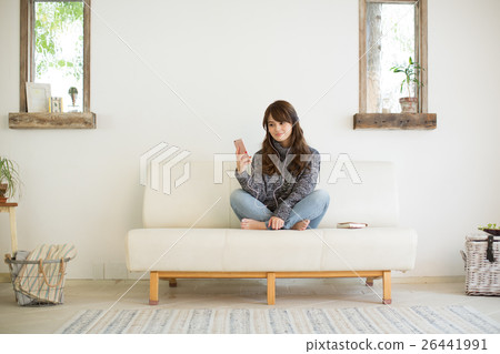 A young lady listening to music while relaxing on the sofa in the living room A young lady listening to music while relaxing on the sofa in the living room 26441991