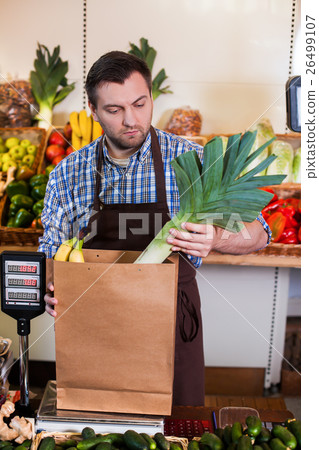 Seller in apron puts purchases in a package. 26499107