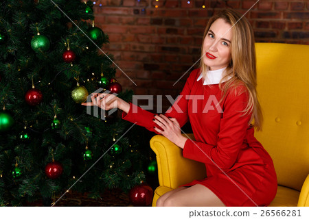 woman in a red dress sits near Christmas tree 26566281