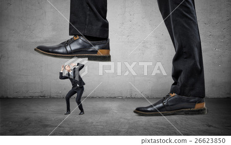 Tiny frightened businessman under feet of huge man 26623850