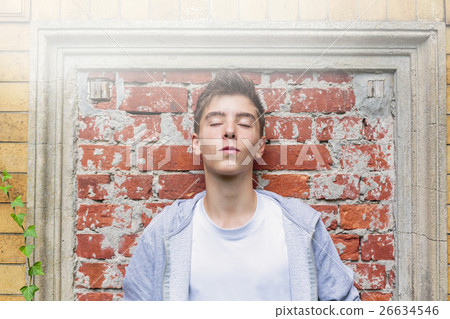 portrait of a teenage boy leaning against a wall, with closed ey 26634546