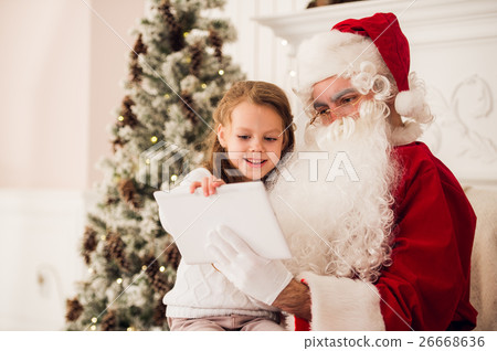 Little girl sitting with Santa using tablet on the 26668636