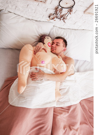 Smiling man lying in bed with rubber sex doll. Stock Photo