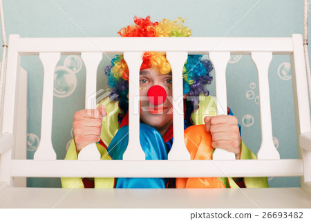 Punished clown sits under a bench. 26693482