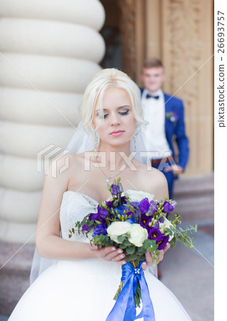 Blond bride with bouquet in hand, in the background in a blue suit Blond bride with bouquet in hand, in the background in a blue suit 26693757