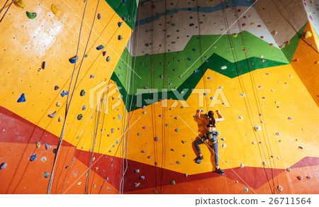 Confident woman climbing up the orange wall in gym Confident woman climbing up the orange wall in gym 26711564