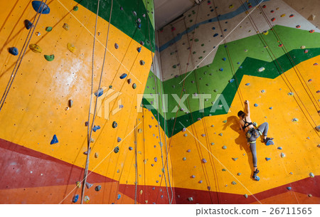 Fearless woman climbing up the orange wall in gym Fearless woman climbing up the orange wall in gym 26711565
