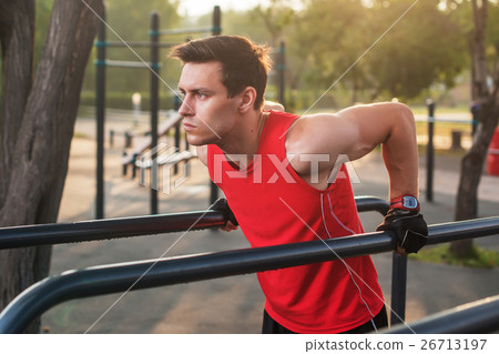 Fit man workout out arms on dips horizontal bars 26713197