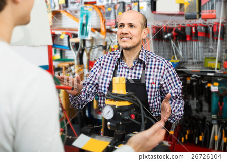 Mature seller showing customer electric compressor in household store Mature seller showing customer electric compressor in household store 26726104