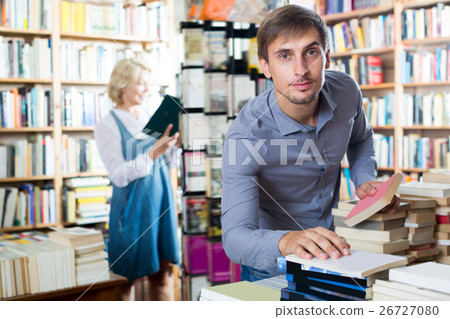Young happy man choosing new book from many Young happy man choosing new book from many 26727080