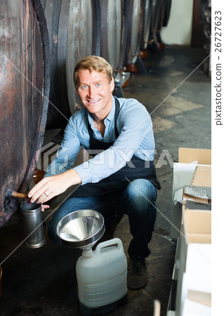man pouring wine from wood in cellar . 26727623