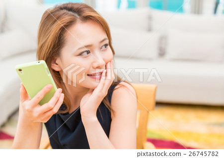 看智能手機的婦女在屋子裡 看智能手機的婦女在屋子裡 26745782