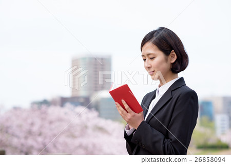 New employee's female business woman confirming the notebook with cherry blossoms behind New employee's female business woman confirming the notebook with cherry blossoms behind 26858094