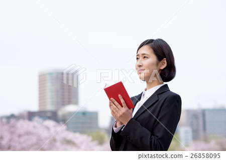 New employee's female business woman confirming the notebook with cherry blossoms behind New employee's female business woman confirming the notebook with cherry blossoms behind 26858095