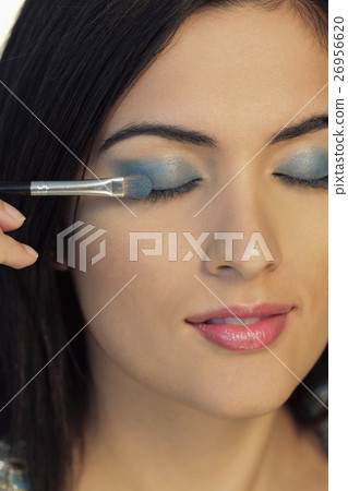 Head shot of young woman putting on blue eyeshadow 26956620