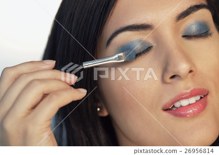 Head shot of young woman putting on blue eyeshadow Head shot of young woman putting on blue eyeshadow 26956814