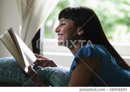 Young woman laying on stomach reading a book and smiling Young woman laying on stomach reading a book and smiling 26956884