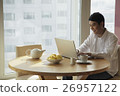 Young man sitting at a table working on a laptop computer 26957122