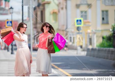 Happy young women with shopping bags walking along 26971015