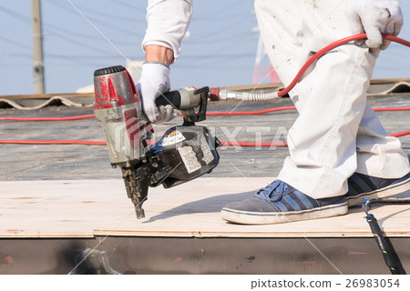 A worker striking a nail with a nail gun on a roof control 26983054