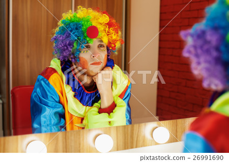Circus clown looks in a mirror in makeup room. Circus clown looks in a mirror in makeup room. 26991690