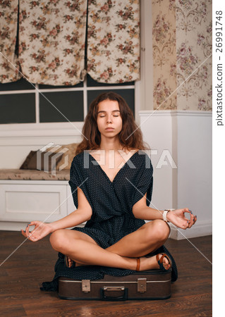 Young woman sits in a pose of yoga on suitcase. 26991748