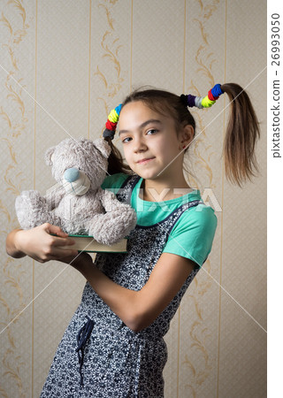 girl holding a book and teddy bear 26993050
