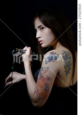 Tattoo asian woman artist holding tattoo machine on dark backgro 27020503
