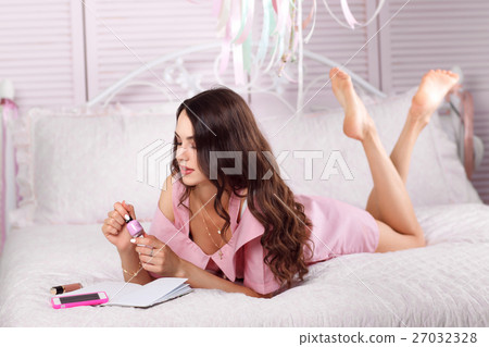 Barefoot woman looking at nail polish on her bed Barefoot woman looking at nail polish on her bed 27032328