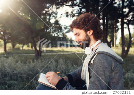 Young man writing in notebook at nature, side view Young man writing in notebook at nature, side view 27032331
