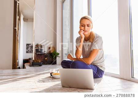 Blond girl using computer in her apartment Blond girl using computer in her apartment 27088878