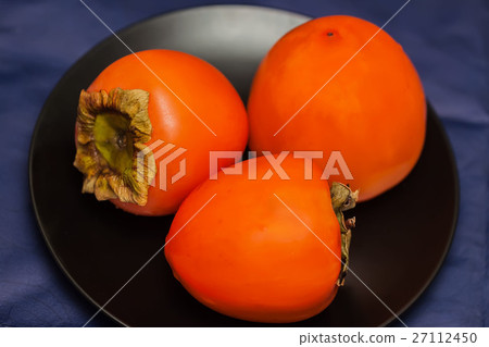 Ripe persimmon fruits in black plate, low key.This Ripe persimmon fruits in black plate, low key.This 27112450