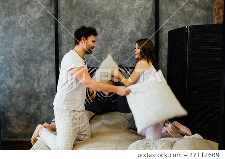 happy couple having pillow fight in bed at home happy couple having pillow fight in bed at home 27112609