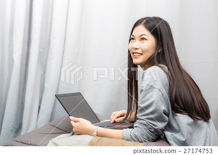 Young lady sitting on bed uing lapt 27174753