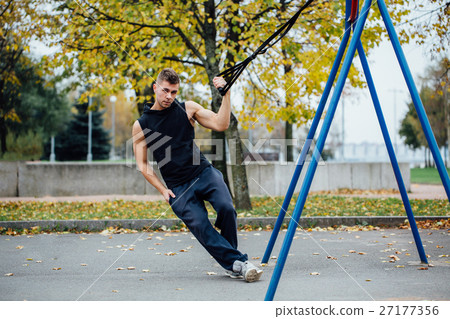 TRX training. Man Instructor at the park doing TRX training. Man Instructor at the park doing 27177356