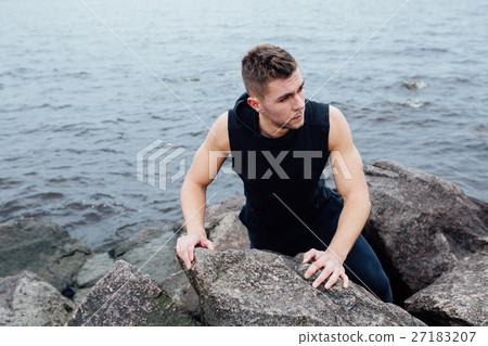 Strong man acts yoga on the rocks beach in the Strong man acts yoga on the rocks beach in the 27183207