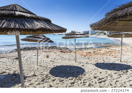 woven umbrellas above rows of many relaxing beds 27224174