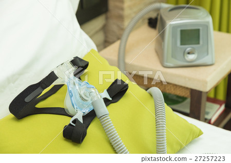 CPAP headgear mask with air tube and machine in bedroom 27257223