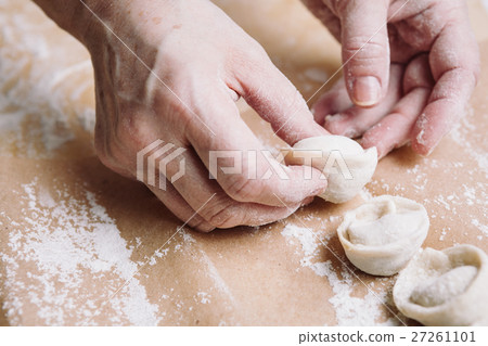 woman folds the raw dumplings on a sheet of 27261101