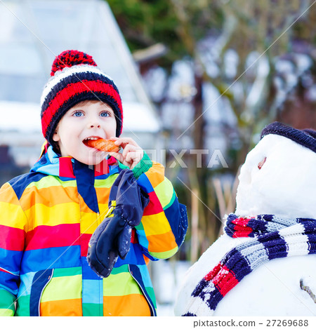 Funny kid boy in colorful clothes making a snowman Funny kid boy in colorful clothes making a snowman 27269688