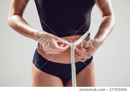 Athletic slim woman measuring her waist by measure 27305666