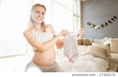 Pregnant woman demonstrating baby clothes Pregnant woman demonstrating baby clothes 27309259