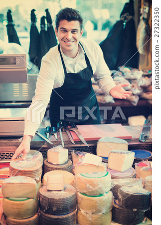 Smiling male seller offering assortment of cheese 27322350