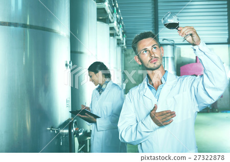 Man worker standing with glass of wine in fermenting section on Man worker standing with glass of wine in fermenting section on 27322878