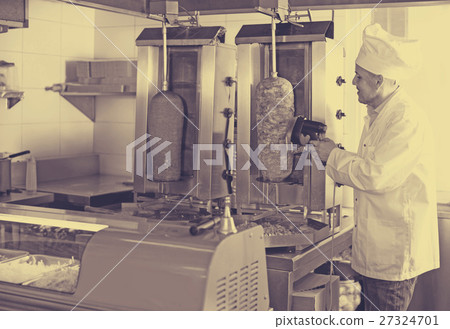 man chef wearing uniform cutting meat for kebab on kitchen in fa man chef wearing uniform cutting meat for kebab on kitchen in fa 27324701