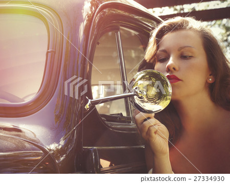 female is fixing her make-up near the vintage car 27334930